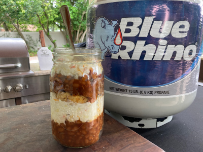 Finished sundae in a mason jar on a wood cutting board, sitting on a black table with a fresh Blue Rhino propane tank and standup propane grill in the background.
