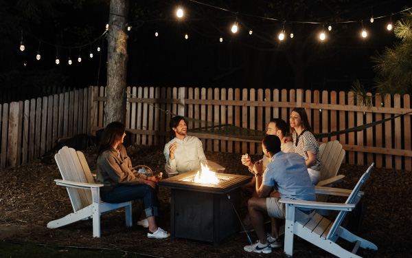 Group of friends sitting in the backyard at night around a lit propane fireplace.