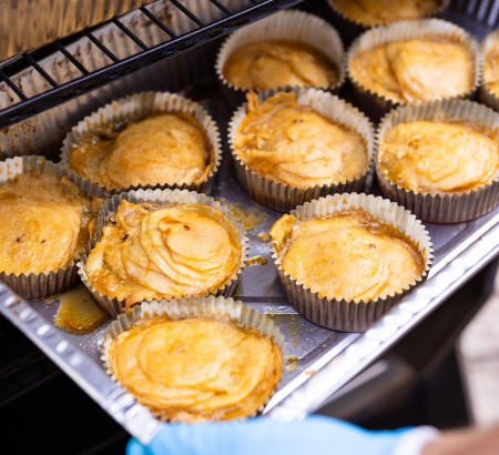 Closeup of grilled cup cakes in an aluminum tray being removed from a smoker.