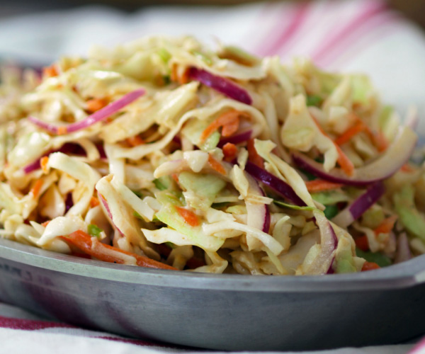 Coleslaw sitting in a gray plate on a red and white tablecloth.