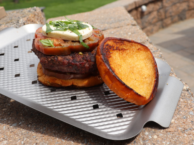 Burger on an aluminum tray sitting on stone surface.