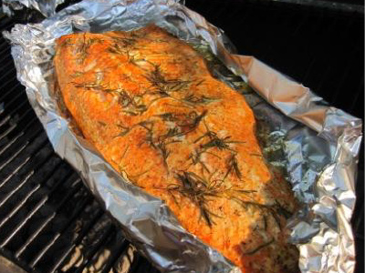 Salmon filet in on aluminum foil on a standup propane grill's cooking grid.