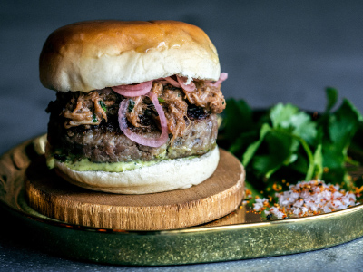 Finished burger on a wood plate on a green tray, sitting on a gray table.