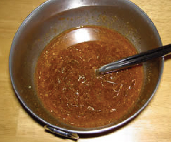 Finished marinade in a stainless steel bowl, with a spoon in it, sitting on a wood table.