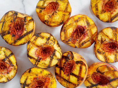 Grilled halves of multiple peaches on a white table.