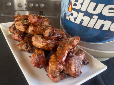 Finished Backyard Party Ribs on a white plate, with a fresh Blue Rhino propane tank and standup propane grill in the background.