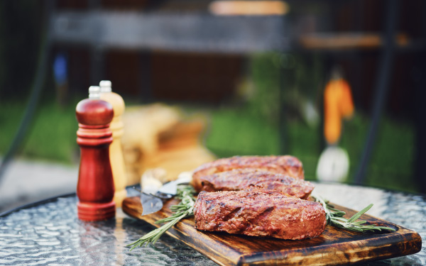 Two finished grilled steaks on a wood plank sitting on a an outdoor patio table.