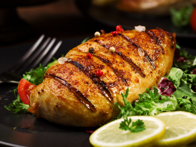 Grilled chicken on black plate with a little salad and lemon slices.