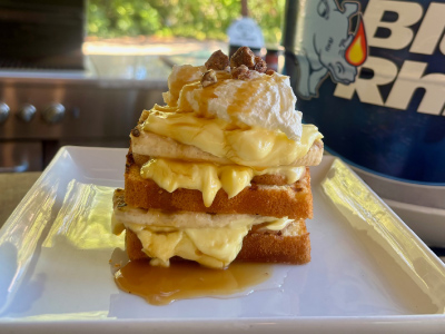 Finished Grilled Banana Pudding on a white plate, with a fresh Blue Rhino and standup propane grill in the background.