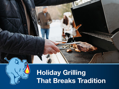 A man wearing winter clothes outside on the patio with snow in the background, opening the lid on a standup propane grill.