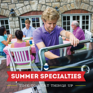 Man in purple polo lifting up the lid of a standup propane grill on a patio, with family in the background.