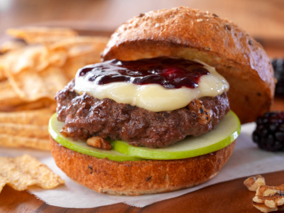 Finished burger on a parchment paper with chips on a wood cutting board.