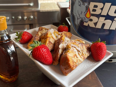 Finished Stuffed French Toast on a white plate, sitting on a wooden cutting board, with a fresh Blue Rhino and a standup propane grill in the background.