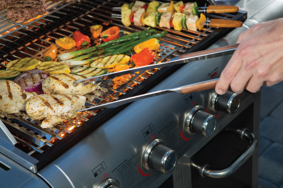 Man using tongs to flip food on a standup propane grill.