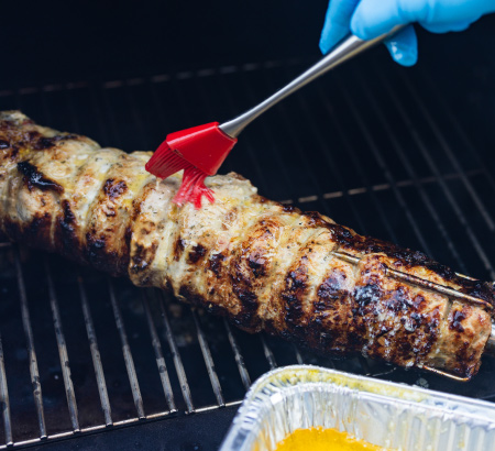 Basting butter on a grilled pork loin on a grill.