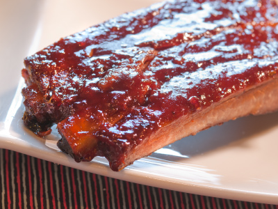 A couple of grilled ribs with blackberry jalapeño sauce on a white plate.