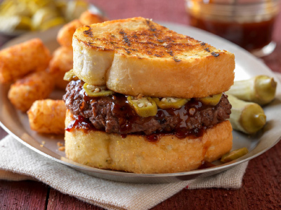 Burger on a stainless steel plate with tator tots, on a table. 