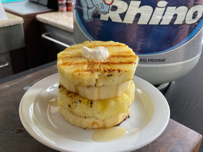 Finished pineapple honey cake on a round white plate, sitting on a table. Fresh Blue Rhino propane tank and standup propane tank in the background.