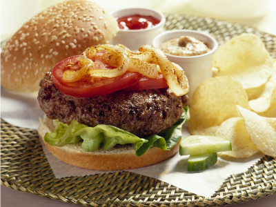 Finished burger with chips and dipping sauce on parchment paper on a wicker plate.