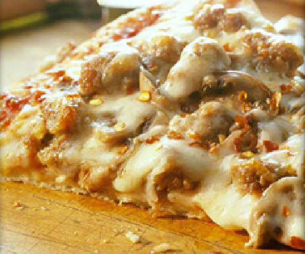 Slice of finished grilled pizza on a wood cutting board.