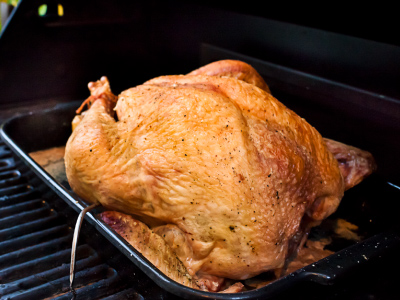 Grilling turkey in a cooking pan sitting on a standup propane grill's cooking grids.