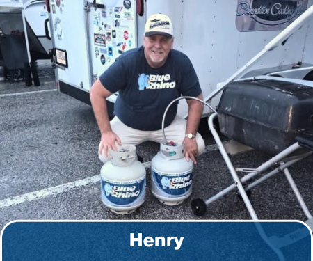 A man crouching down in front of two Blue Rhino tanks connected to a propane grill.