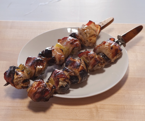 Two grilled kabobs on a white plate, sitting on a wood table.