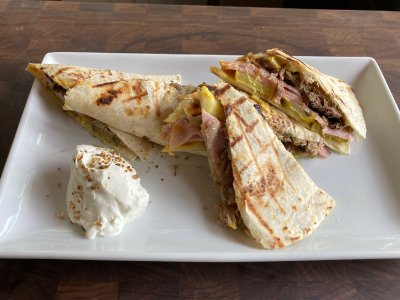 Grilled quesadilla sliced into quarters and stacked on top of each other and a dollop of sour cream on a rectangular white plate, sitting on a wooden table.