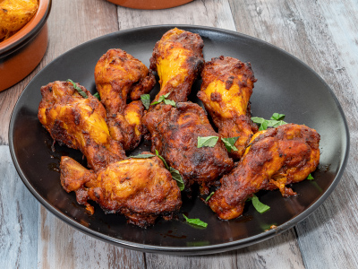 Finished peri peri chicken legs on a black plate sitting on a wooden table.