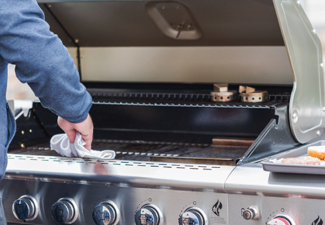 A man outside cleaning the cooking grates on his stainless steel standup propane grill.