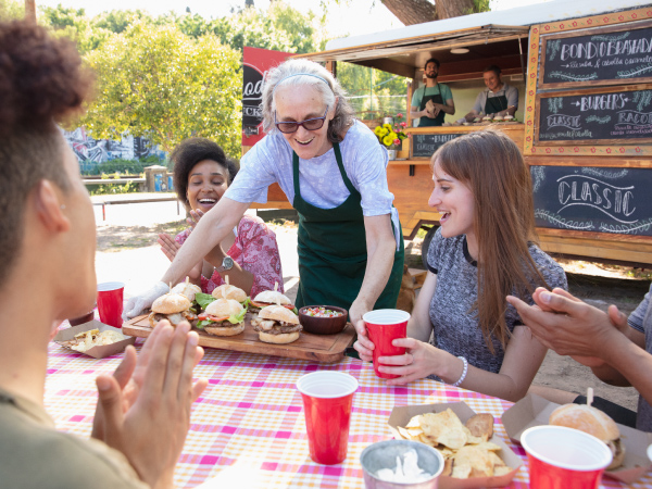 Friends sitting at a table, with food being served from a food truck.