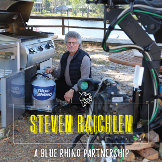 A behind the screen photo of Steven Raichlen inserting a fresh Blue Rhino propane tank into a stainless steel standup propane grill.