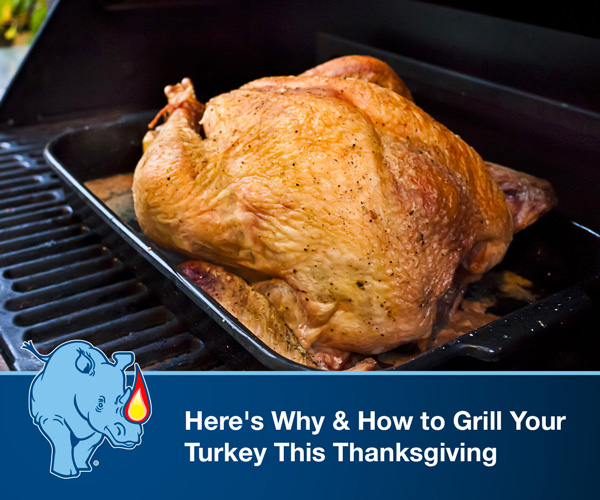 Turkey in a black pan being grilled on a standup propane grill.
