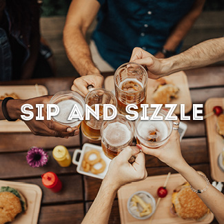 A top view of friends cheering with beer glasses over a wooden table with burgers on them.
