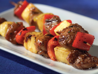 Two grilled skewers on a white plate, sitting on a blue tablecloth.