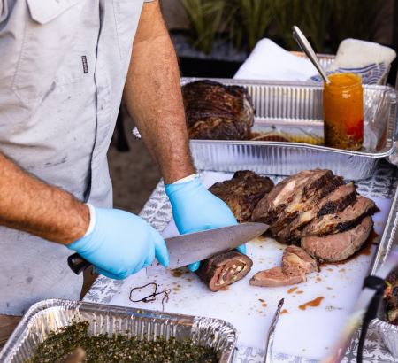 Chef cutting up a freshly grilled pork loin on a cutting board.