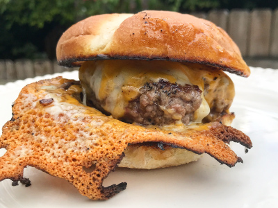 Finished grilled burger on a white plate. Backyard in the background.