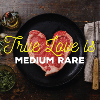 Raw heart shaped steak sitting on a black plate, on a wood table.