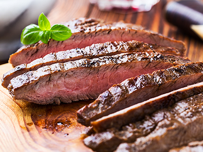 Finished sliced grilled steak sitting on a wooden serving platter.