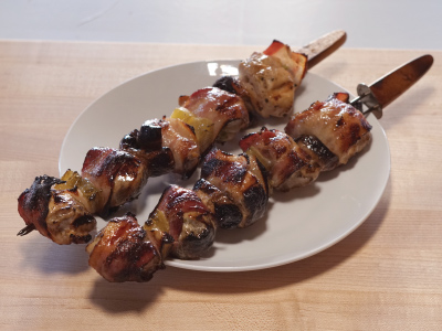 Two grilled kabobs on a white plate, sitting on a wood table.