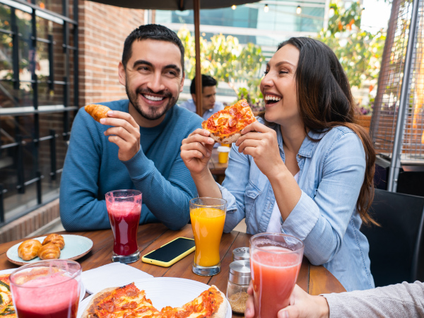 Friends sitting outside at a restaurant eating pizza with a patio heater in the background.