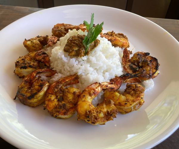Barbecued shrimp circling a mound of rice on a white plate.