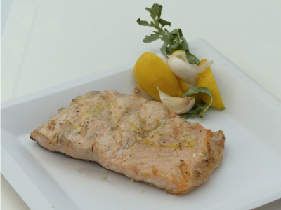 Finished salmon filet with lemon wedges, garlic and rosemary on a white square plate on a white table.