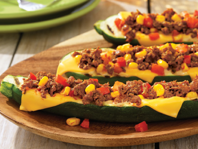 Three finished zucchini boats on a wood serving tray, sitting on a wood table.