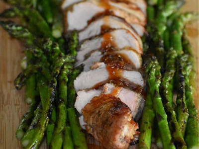 Grilled sliced pork tenderloin with sauce  and grilled asparagus on a bamboo plate.