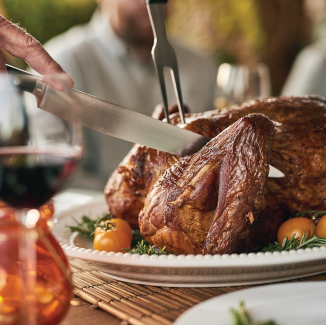 Finished grilled turkey on a white plate on a wooden table, starting to be cut with a knife.