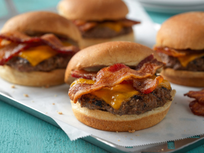 Four finished burgers on parchment paper on a silver serving tray, sitting on a teal tablecloth.
