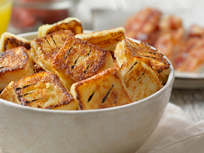 Tan colored bowl filled with french toast bites, on a tan colored tablecloth.