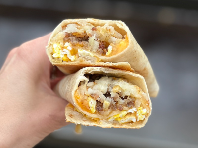 Hand holding a finished burrito that is cut in half gray background.