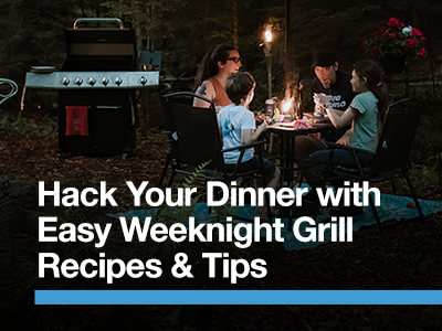 Family outside at night, sitting at a table eating dinner with a standup propane grilling in the background.